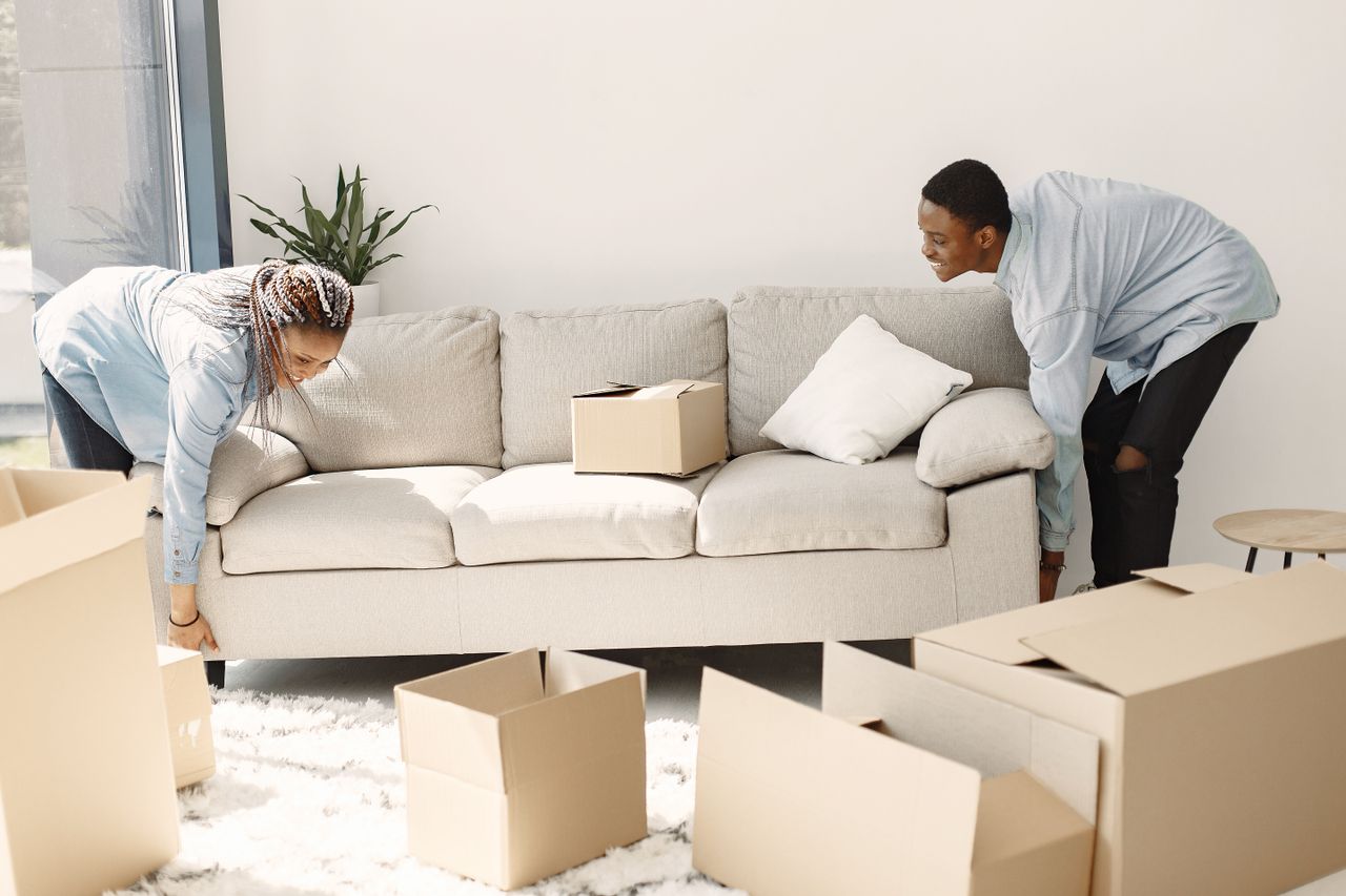 Happy couple setting up a sofa in their new home surrounded by moving boxes.
